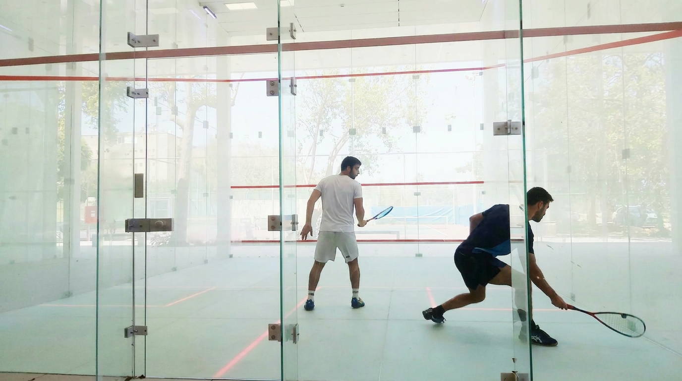 Two players mid-rally inside a Tpoint glass-walled court, surrounded by greenery